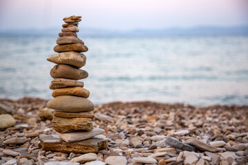 Fototapeta na wymiar Pebbles tower balances harmony stones on the Aegean sea coast at sunset. Relaxing spa tranquility concept 