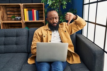 African american man using laptop at home sitting on the sofa with angry face, negative sign...