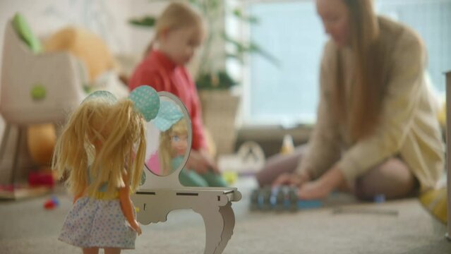 Doll stands at the toy table mirror, mother and daughter playing busily at nursery room background, nice casual interior, games on the floor. Family playtime delight, active imagination.HQ 4k footage