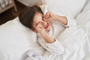 Adorable hispanic girl lying on bed waking up at bedroom