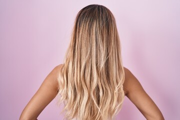 Fototapeta premium Young blonde woman standing over pink background standing backwards looking away with arms on body