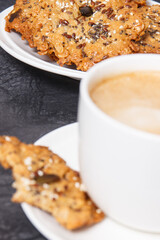 Cup of white coffee and fresh baked oatmeal cookies with honey and healthy seeds. Delicious crunchy dessert