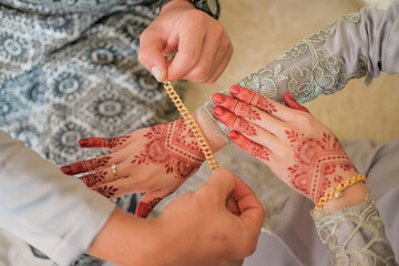 The groom is dressing the bracelet to the bride's hand during the Malay wedding ceremony in Malaysia. The bride’s hand with henna.
