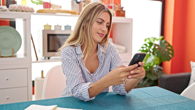Young blonde woman using smartphone sitting on table at dinning room