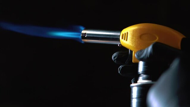 Close-up of a chef's hand in a sterile black glove emitting fire from a gas burner for cooking.