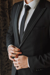 young man fastens his jacket in his hands in his room, near the window in the hotel room, young businessman, close-up photo. The groom is preparing for the wedding ceremony