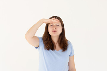 Portrait of curious woman in blue t-shirt holding hand above eyes and peering into distance, looking far away, expecting and searching someone on horizon
