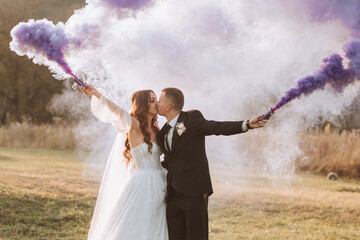 brides play with colored smoke in purple hands. Smoke bombs at a wedding.