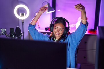 Young beautiful hispanic woman streamer playing video game with winner expression at gaming room