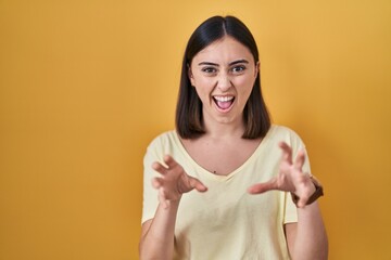 Hispanic girl wearing casual t shirt over yellow background smiling funny doing claw gesture as...