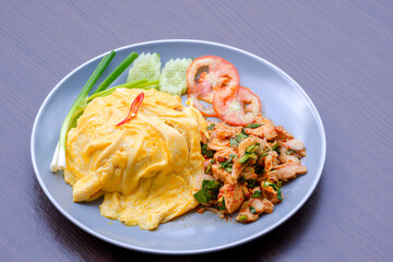 Creamy Omelet on Rice with spicy sliced grilled pork salad and vegetable in gray ceramic dish on wooden table