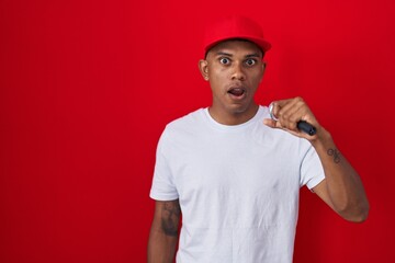 Young hispanic man singing song using microphone scared and amazed with open mouth for surprise, disbelief face