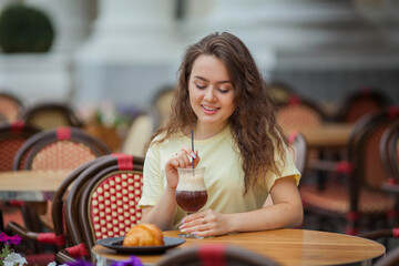 Beautiful dark-haired young curly woman sits in summer cafe and drinks coffee cocktail. Warm. Rest.