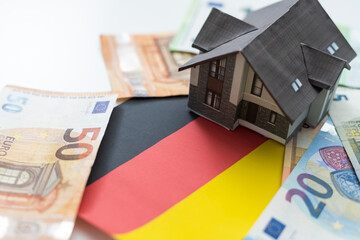 Real estate concept. On the flag of Germany there is a model of a wooden house with the inscription...