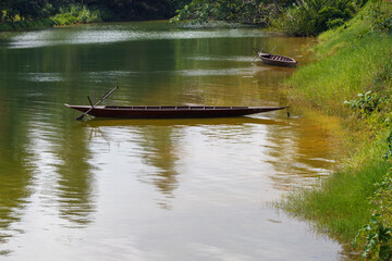 A landscape photo of a lake with one wooden boat. the photo has a lot of green color and has a lot of green scenery
