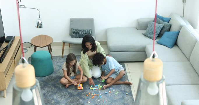 Friendly Brazilian Babysitter Play Plastic Building Blocks With Little Siblings Sit On Floor In Living Room, View From Top. Multinational Family Enjoy Pastime, Playtime At Home, Motherhood, Custody