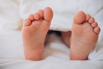 
bare feet of a child under a white blanket on the bed in the morning