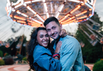 Boyfriend and girlfriend looking at camera while embracing in amusement park