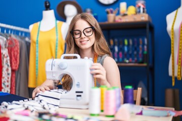 Young woman tailor smiling confident using sewing machine at clothing factory