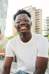 Vertical portrait of a smiling cheerful young African american student with a positive smile, white perfect teeth, looking at camera sitting outside taking a break at the university. High quality