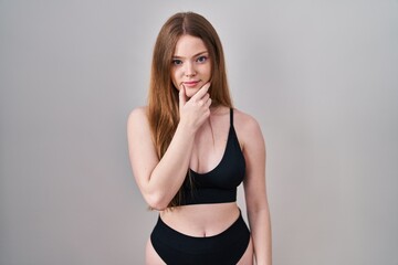 Young caucasian woman wearing lingerie looking confident at the camera with smile with crossed arms and hand raised on chin. thinking positive.