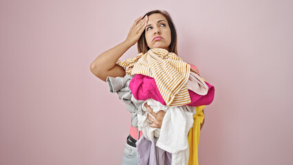 Middle eastern woman holding dirty clothes looking upset over isolated pink background