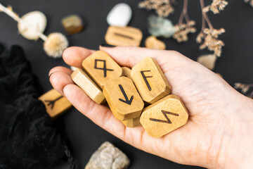 Stack of wooden runes in hand on black table background. Scandinavian magical esoteric symbols and...