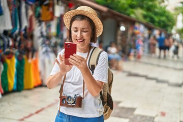 Middle age woman tourist smiling confident using smartphone at street market