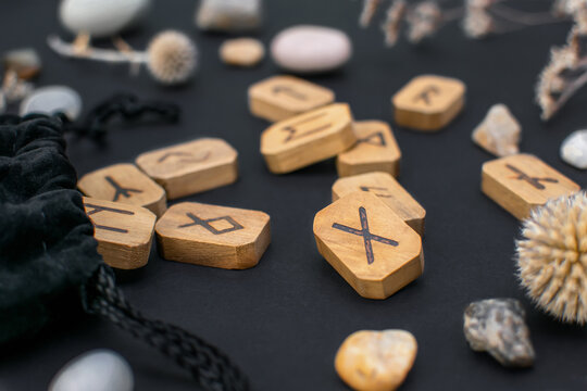 Textile bag with stack of wooden runes and stones on a black table. Scandinavian magical esoteric symbols and signs for divination and prediction of the future and destiny are cut out of wooden bars.