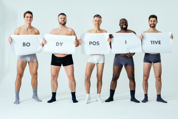 multiethnic men posing for a male edition body positive beauty set showing messages on banners....
