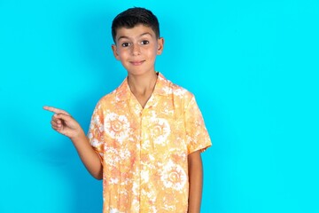 Little hispanic boy wearing hawaiian shirt  points to side on blank space demonstrates advertisement. People and promotion concept