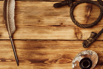 Feather pen and inkwell on wooden background top view