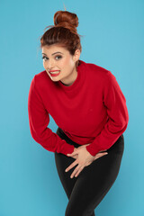 Redhead woman suffering from pain and holding her hands in the lower abdomen on a blue background