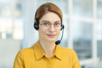 Portrait of successful smiling business woman with headset phone, mature experienced worker smiling...