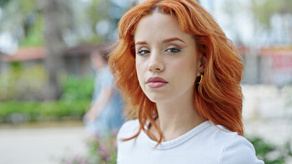 Young redhead woman standing with relaxed expression at park