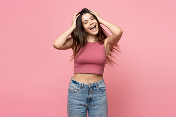 Portrait of smiling teenage girl with long hair, closed eyes standing isolated on pink background