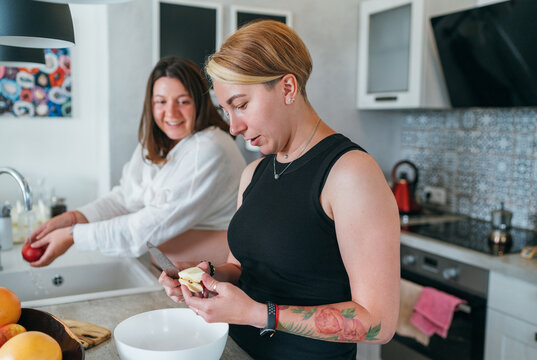 Two smiling females cooking a dinner in the kitchen. Same-sex marriage couple in the home interior. Woman's health, happy pregnancy doula supporting and calm mental mood concept image.