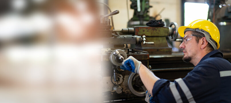 Professional caucasian white ethnicity male technician operating the heavy duty machine in the lathing factory. Technician in safety and helmet suit controlling a machine in factory.