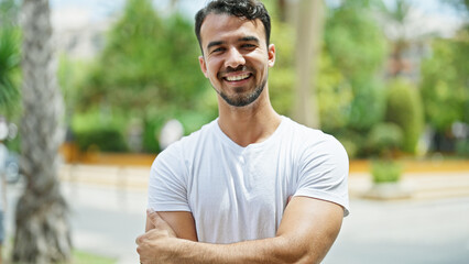 Young hispanic man smiling confident standing with arms crossed gesture at park