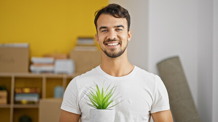 Young hispanic man smiling confident holding plant pot at new home