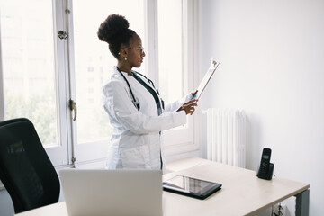 Focused black woman doctor standing with clipboard in room