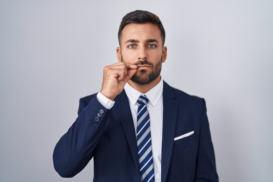 Handsome hispanic man wearing suit and tie mouth and lips shut as zip with fingers. secret and silent, taboo talking