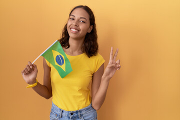 Young hispanic woman holding brazil flag smiling looking to the camera showing fingers doing...