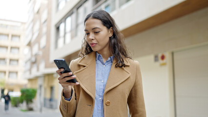Young beautiful hispanic woman using smartphone with serious face at street