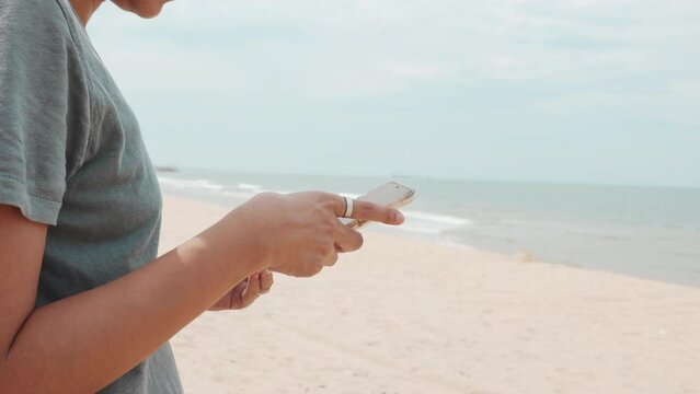 Asian woman on her enjoyable journey of freedom and outdoor enjoyment on the beach abd sea. With smartphone in hand, she captures moments of happiness, sharing them in the digital social network.