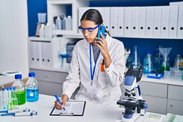 Young african american woman scientist talking on the smartphone write on report document at...