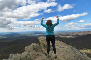 Obraz premium Middle-age woman standing on rock ledge arms in air celebrating success, victory