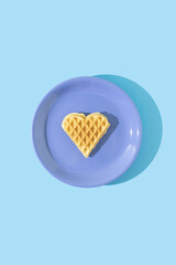 Freshly baked homemade heart shape waffle on ceramic plate. Minimal concept of sweet food and love. Flat lay. Light blue background.