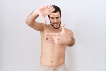 Fototapeta premium Young hispanic man standing shirtless over white background smiling making frame with hands and fingers with happy face. creativity and photography concept.