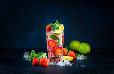Summer strawberry mojito cocktail with lime, white rum, soda, cane sugar, mint, and ice in glass on deep blue background. Cold refreshing beverage